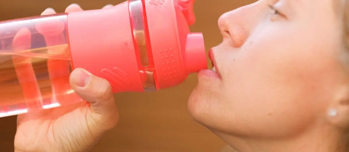 Persona bebiendo de una botella de plástico rosa
