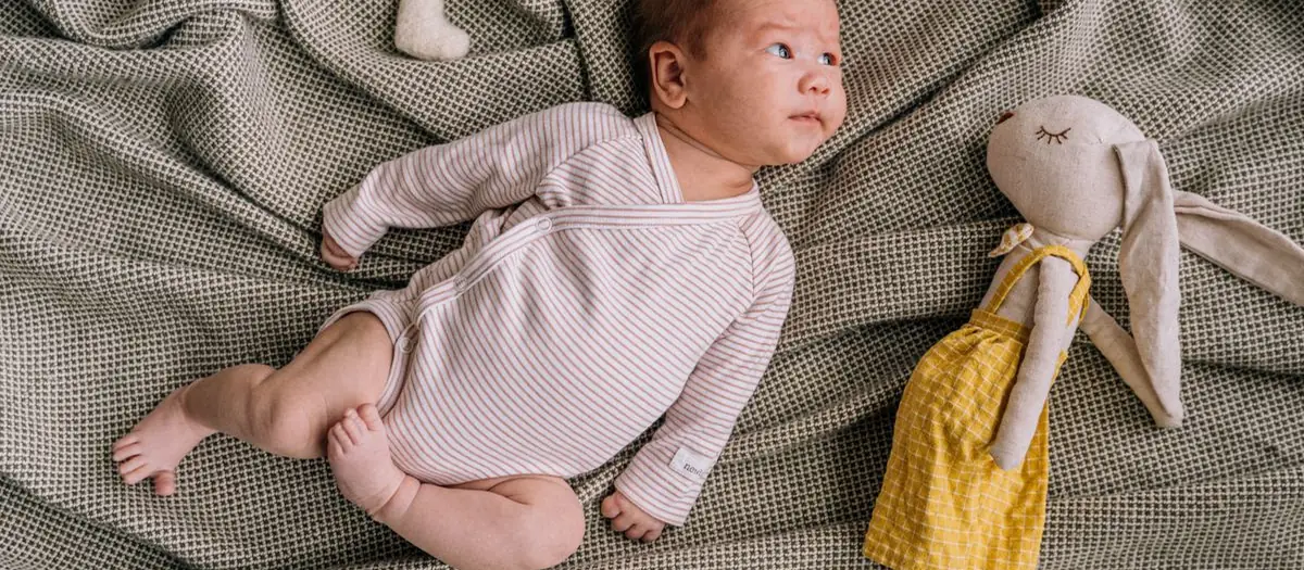 Bebé tumbado junto a un muñeco de tela